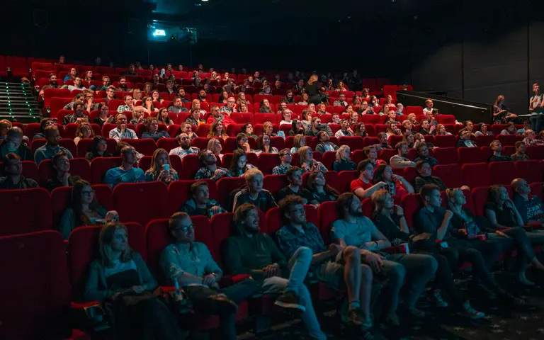 Puna bioskopska sala sa crvenim sedištima u polumraku